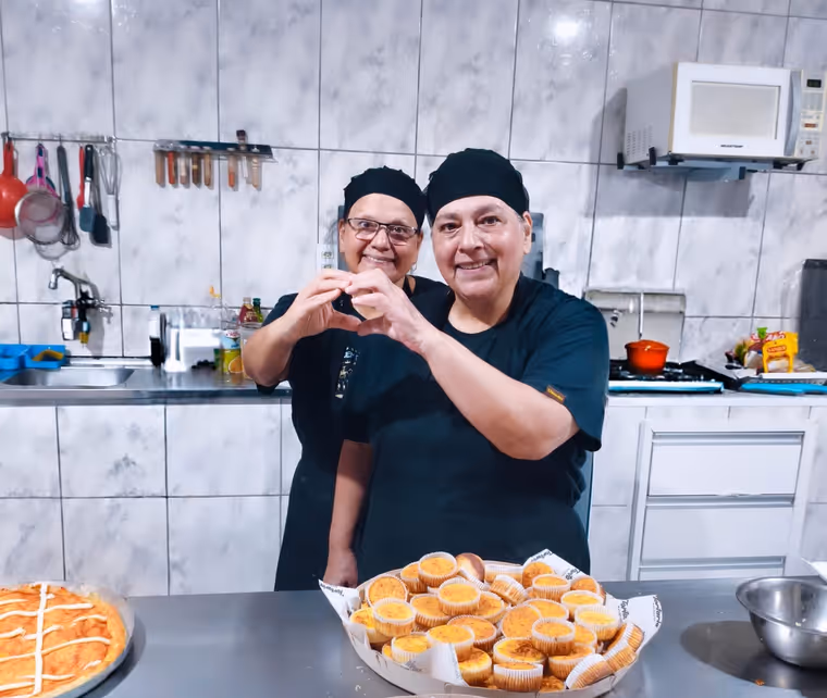 Magali e Roseli, as gêmeas que comandam a Tortaria Estância, fazendo um coração com as mãos na cozinha