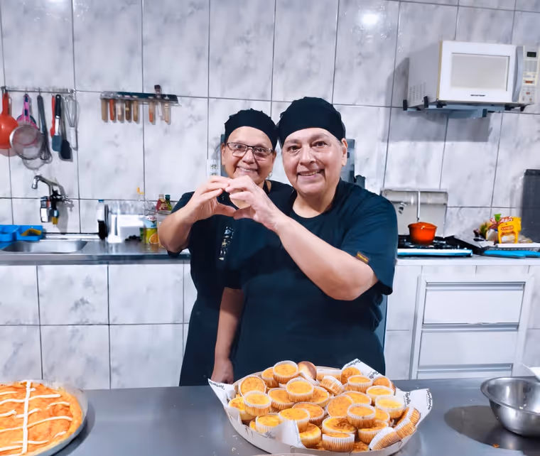 Magali e Roseli, as gêmeas que comandam a Tortaria Estância, fazendo um coração com as mãos na cozinha